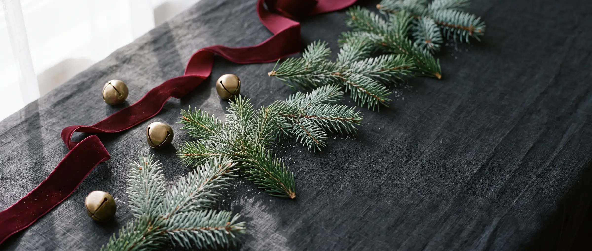 Evergreen branches, burgundy velvet ribbon and brass jingle bells on a dark surface (illustrative image)